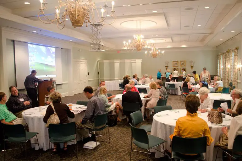 A group of people sitting at tables in front of a projector screen.