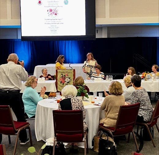 A group of people sitting around tables in front of a projector screen.
