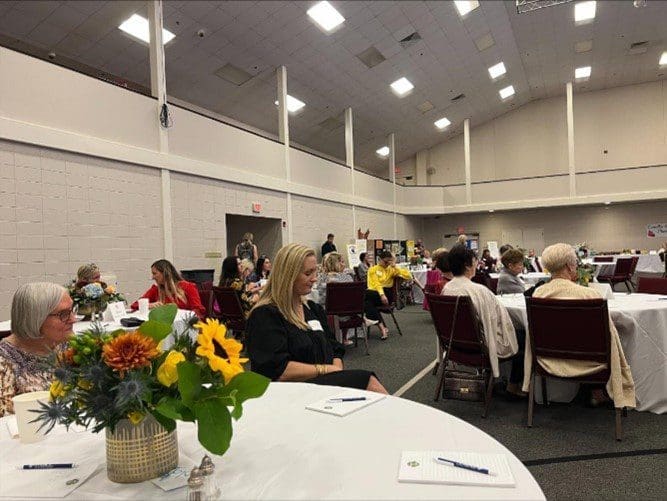 A group of people sitting at tables with flowers.