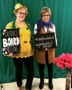 Two women holding signs in front of a green background.