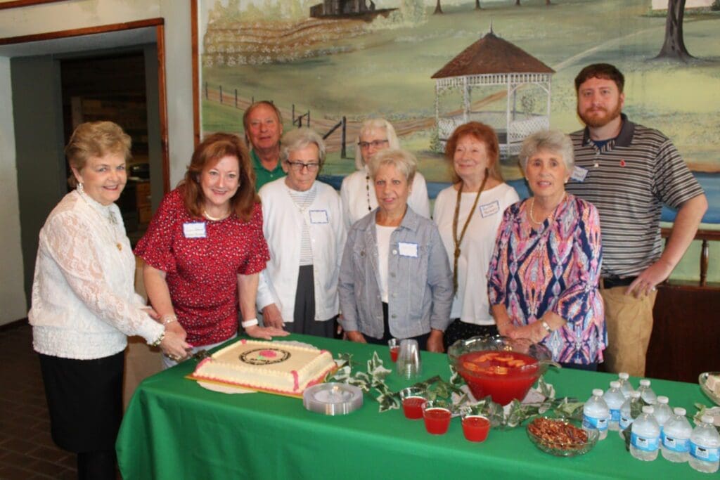 A group of people standing around a table with cake.