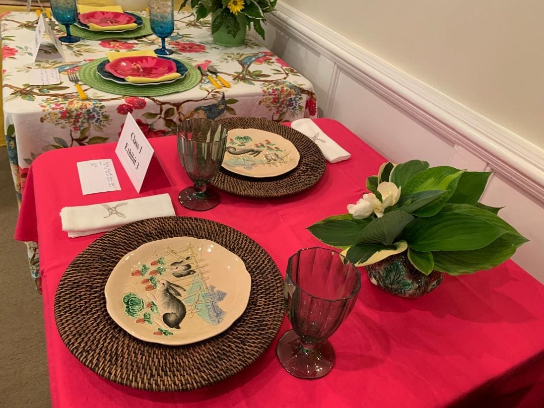 FlowershowII042023 A table set with plates and glasses on top of red cloth.