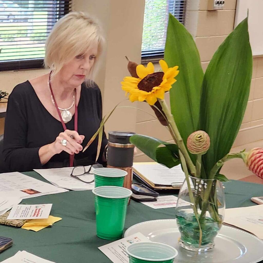 A woman sitting at a table with a vase of flowers.