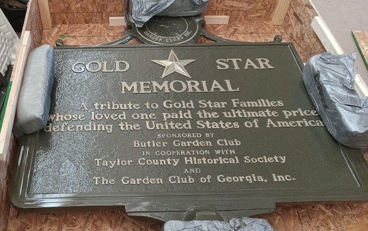 A plaque that is on the ground in front of trees.