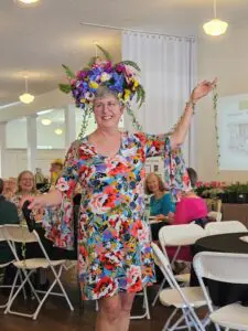 A woman in floral dress and hat standing next to chairs.