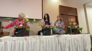 Three women sitting at a table with flowers.