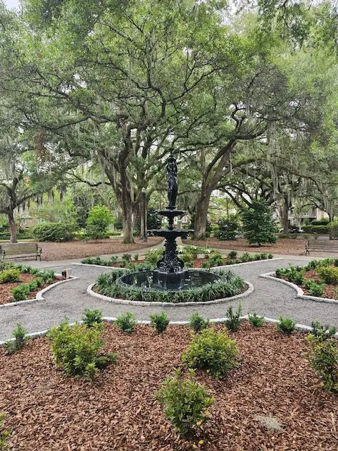 A fountain in the middle of a park surrounded by trees.