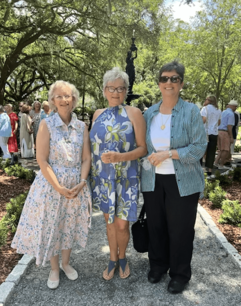 Three women standing in a garden with trees.