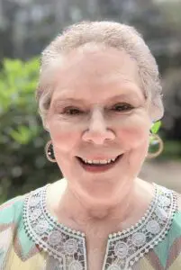Bonnie Dudley May 2025 A smiling elderly woman wearing hoop earrings and a light-colored top.