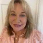 A smiling woman with blonde hair wearing a pink top.