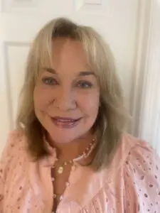 A smiling woman with blonde hair wearing a pink top.