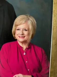 A smiling woman in a red blouse with blonde hair.