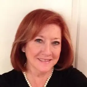 Jan C Stewart A smiling woman with red hair wearing a black top and pearl necklace.