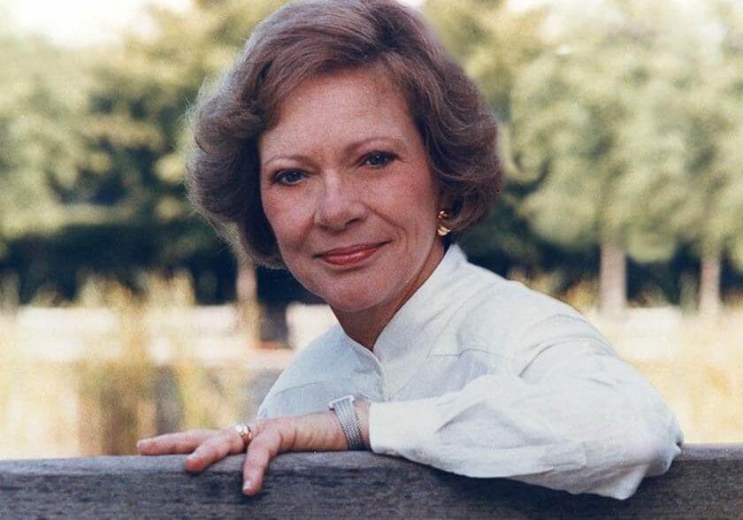 37-Rosalynn-Carter-portrait-1993 A woman leaning on a wooden fence in front of trees.