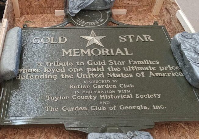 Gold Star Marker Butler A plaque that is on the ground in front of trees.